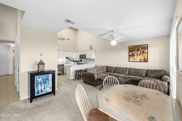 living room with a textured ceiling, visible vents, ceiling fan, vaulted ceiling, and light carpet