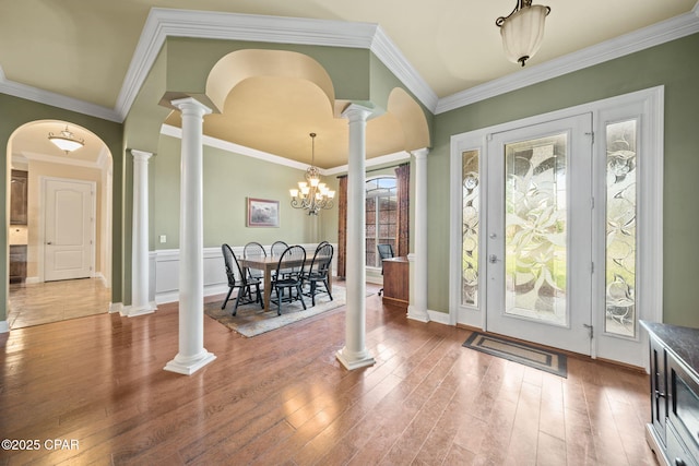 entryway featuring ornamental molding, ornate columns, wood finished floors, and a notable chandelier