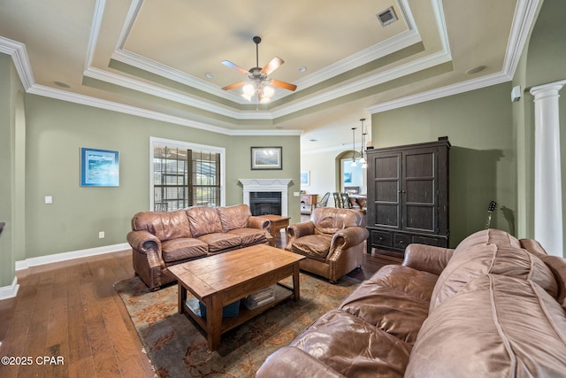 living area featuring crown molding, a fireplace, hardwood / wood-style floors, a ceiling fan, and a tray ceiling