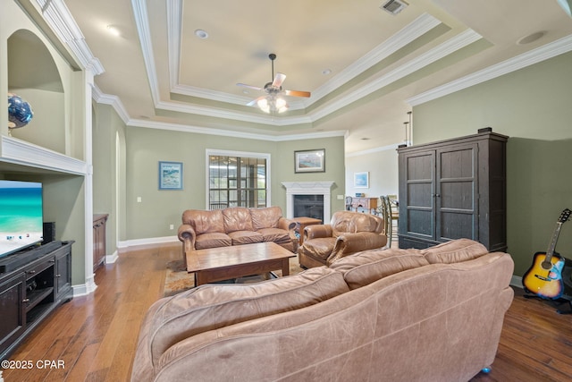 living room featuring crown molding, hardwood / wood-style floors, a fireplace, ceiling fan, and a raised ceiling