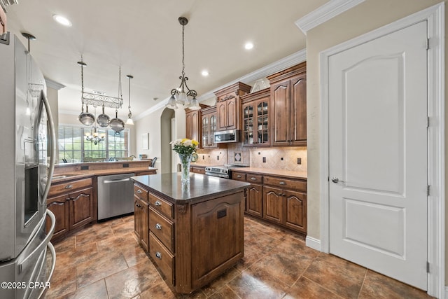 kitchen featuring decorative backsplash, crown molding, appliances with stainless steel finishes, a center island, and dark countertops