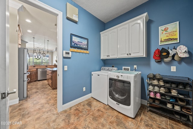 washroom featuring cabinet space, washing machine and clothes dryer, a notable chandelier, stone finish floor, and baseboards
