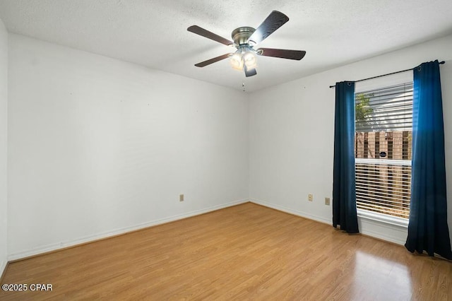 spare room featuring a textured ceiling, light wood-style floors, a ceiling fan, and baseboards