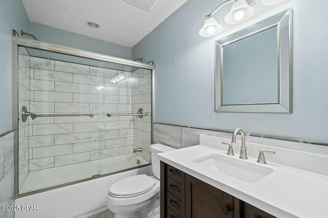 bathroom with a textured ceiling, combined bath / shower with glass door, toilet, tile walls, and vanity