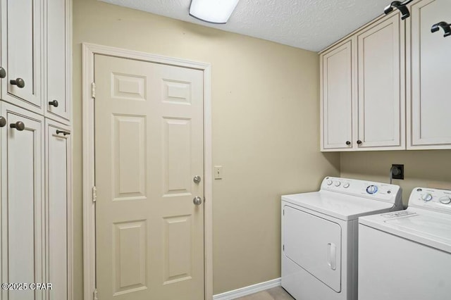clothes washing area featuring a textured ceiling, washing machine and clothes dryer, cabinet space, and baseboards
