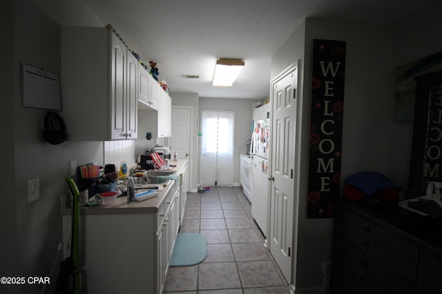 kitchen featuring freestanding refrigerator, light tile patterned floors, light countertops, white cabinets, and visible vents