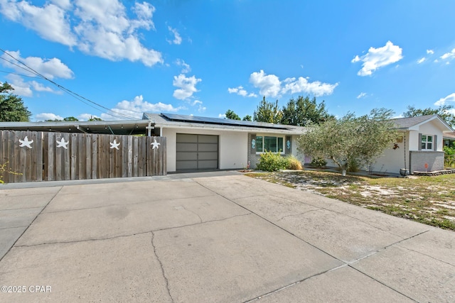 ranch-style home featuring a garage, fence, brick siding, concrete driveway, and solar panels