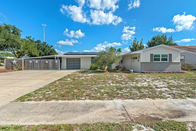 ranch-style house with driveway, a carport, fence, roof mounted solar panels, and stucco siding