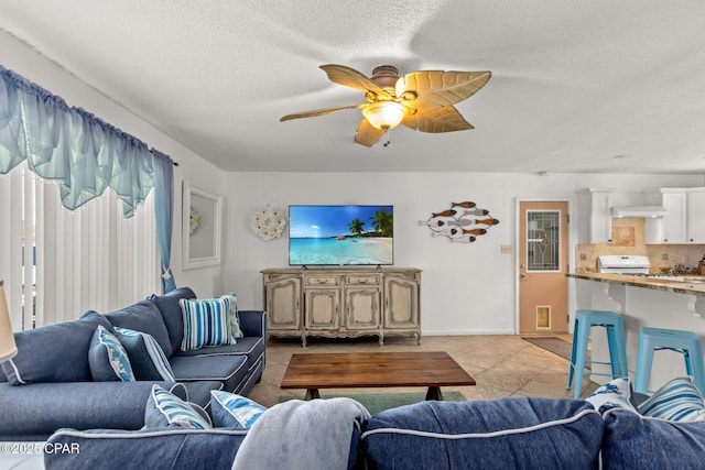 living area with light tile patterned flooring, ceiling fan, baseboards, and a textured ceiling