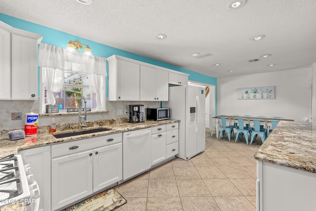 kitchen featuring a sink, white cabinets, backsplash, and white appliances