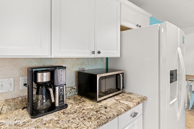 kitchen with light stone counters, white cabinets, white fridge with ice dispenser, and tasteful backsplash
