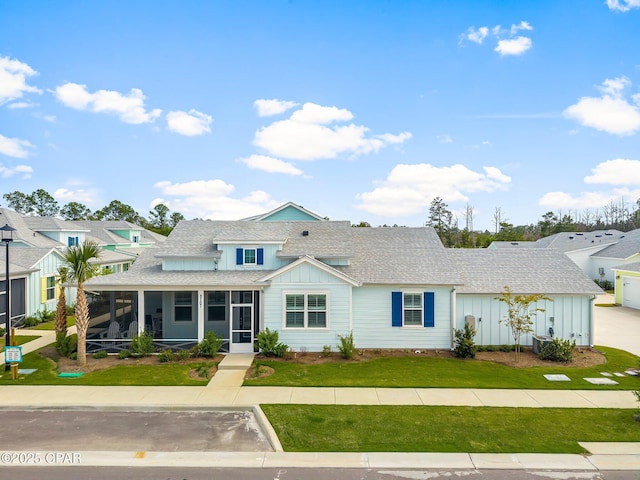 view of front of property featuring roof with shingles, board and batten siding, a sunroom, and a front lawn