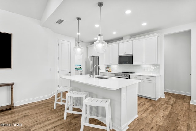 kitchen featuring visible vents, a breakfast bar, an island with sink, a sink, and stainless steel appliances