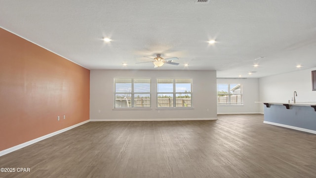 unfurnished living room featuring dark wood-type flooring, a ceiling fan, baseboards, and a sink