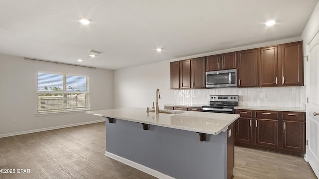 kitchen featuring a sink, stainless steel appliances, a kitchen breakfast bar, tasteful backsplash, and light wood-style flooring