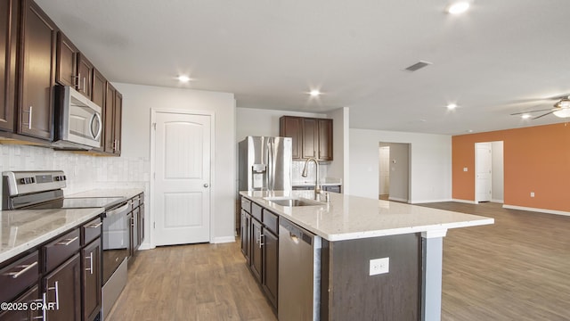 kitchen with appliances with stainless steel finishes, wood finished floors, dark brown cabinetry, and a sink