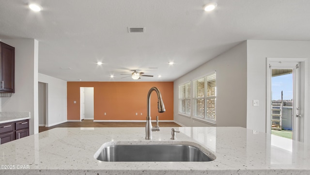 kitchen featuring light stone counters, ceiling fan, a sink, visible vents, and open floor plan