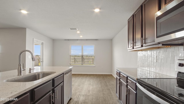kitchen with light wood-style flooring, a sink, appliances with stainless steel finishes, dark brown cabinets, and baseboards