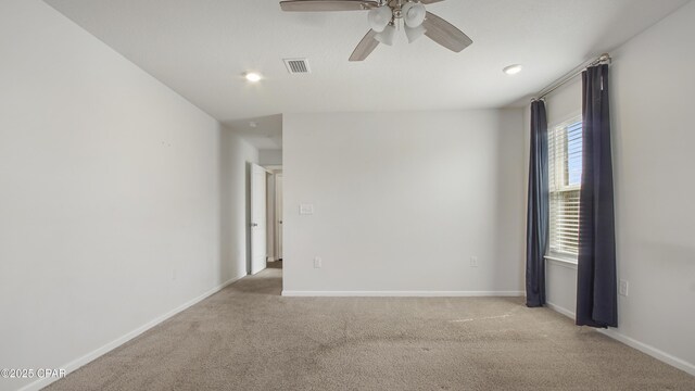 spare room with a ceiling fan, visible vents, light colored carpet, and baseboards