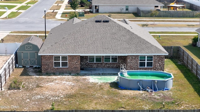 rear view of house featuring brick siding, a fenced backyard, a shingled roof, and a storage shed