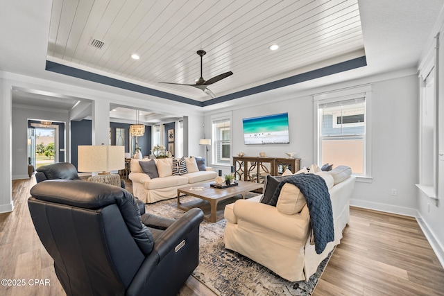 living room with light wood-style flooring, visible vents, a ceiling fan, and a tray ceiling