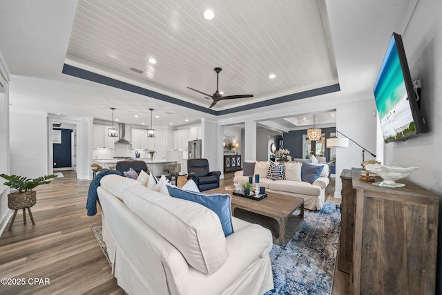 living area with recessed lighting, ceiling fan, light wood-style floors, and a tray ceiling