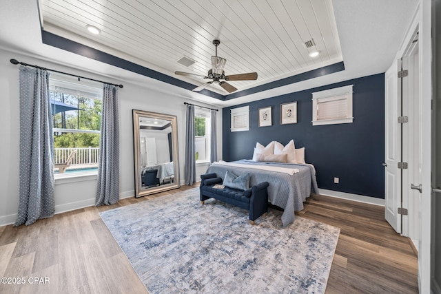 bedroom with wood ceiling, multiple windows, wood finished floors, and a tray ceiling