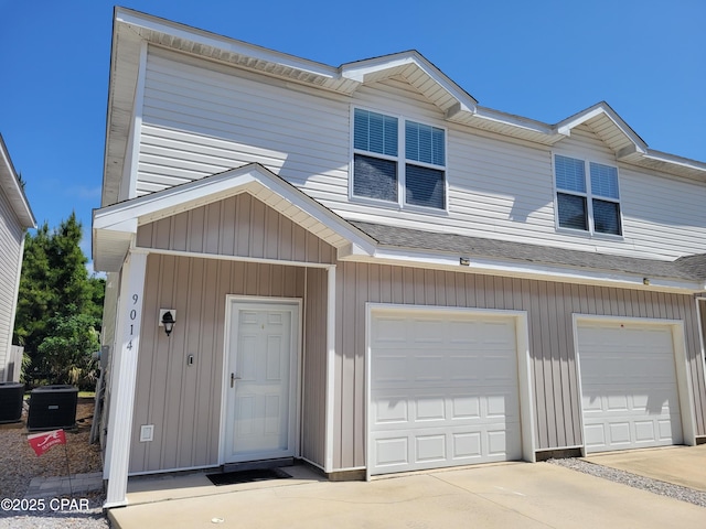 view of property featuring concrete driveway, roof with shingles, central air condition unit, and a garage