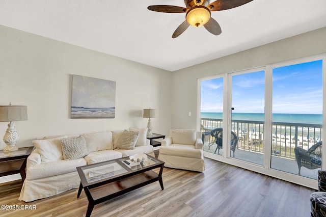 living area with wood finished floors, a ceiling fan, and view of water and beach