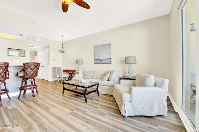 living area with light wood-style floors, ceiling fan, baseboards, and a chandelier