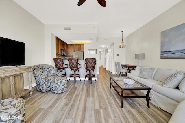 living area with light wood finished floors, a ceiling fan, a chandelier, and baseboards
