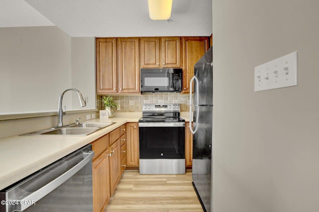 kitchen with stainless steel appliances, a sink, light wood-style floors, tasteful backsplash, and light countertops