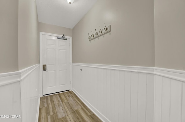 doorway featuring a wainscoted wall, light wood-style floors, and a textured ceiling