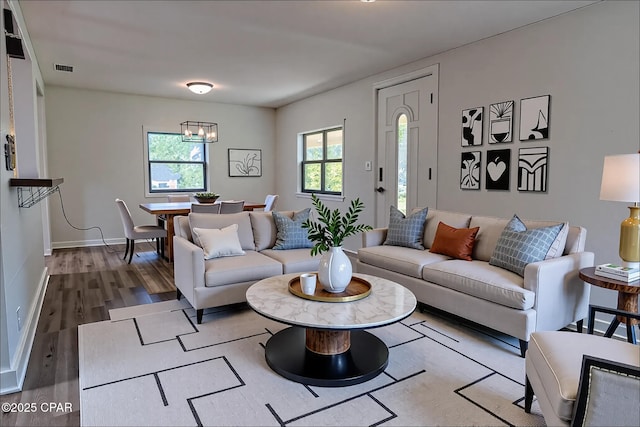 living area with baseboards, wood finished floors, a chandelier, and visible vents