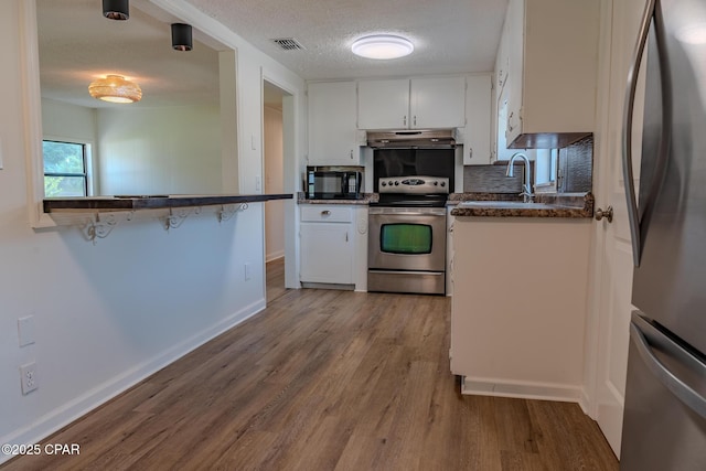 kitchen featuring visible vents, dark countertops, under cabinet range hood, a sink, and appliances with stainless steel finishes