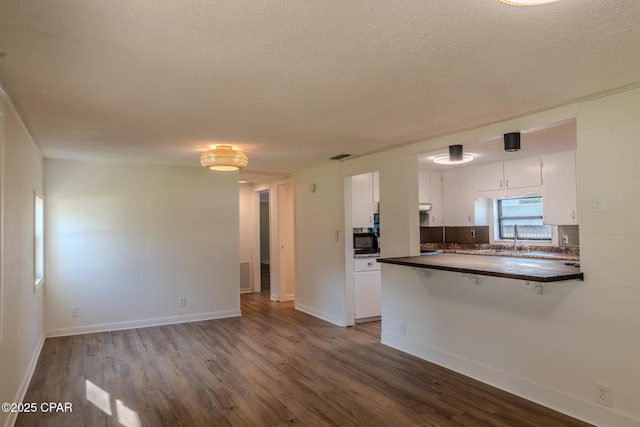kitchen with white cabinetry, dark countertops, black microwave, and wood finished floors