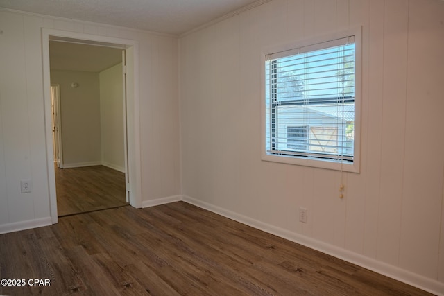 spare room with crown molding, dark wood finished floors, a decorative wall, and baseboards