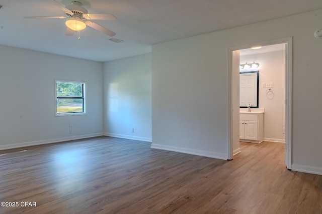 empty room featuring visible vents, wood finished floors, baseboards, ceiling fan, and a sink