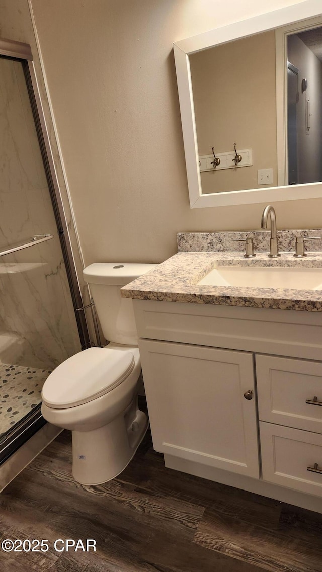 full bathroom featuring toilet, vanity, a marble finish shower, and wood finished floors
