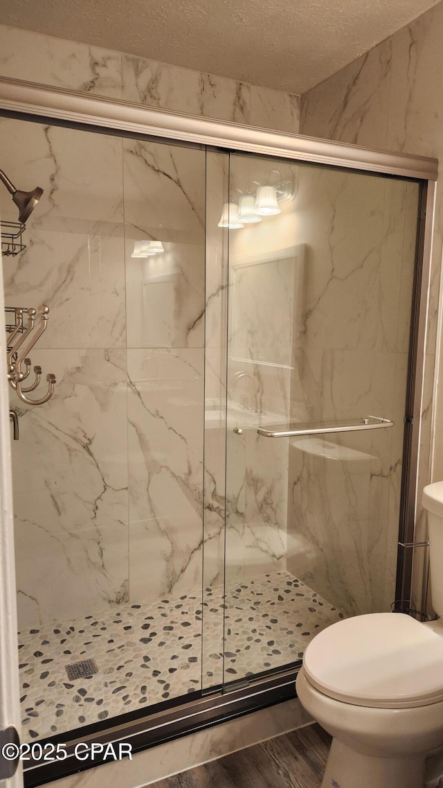 bathroom featuring wood finished floors, a marble finish shower, toilet, and a textured ceiling
