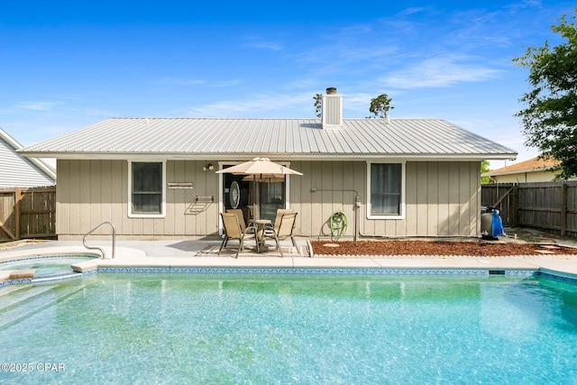rear view of property featuring a patio, a fenced backyard, a chimney, metal roof, and a pool with connected hot tub