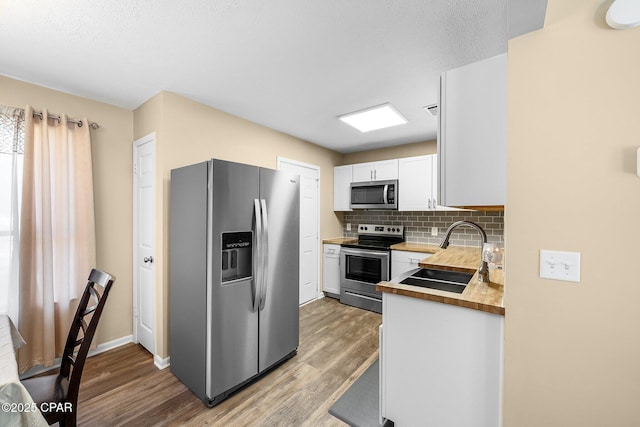 kitchen with decorative backsplash, white cabinetry, a sink, light wood finished floors, and stainless steel appliances