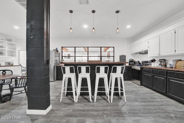 kitchen featuring under cabinet range hood, a kitchen bar, dark cabinetry, white cabinetry, and appliances with stainless steel finishes