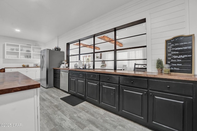 kitchen featuring wood counters, light wood-style flooring, a sink, appliances with stainless steel finishes, and dark cabinetry