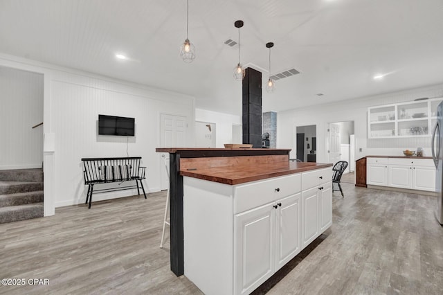 kitchen with white cabinetry, light wood-style flooring, visible vents, a center island, and butcher block counters