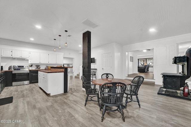 dining area featuring light wood-type flooring, crown molding, a wood stove, and recessed lighting