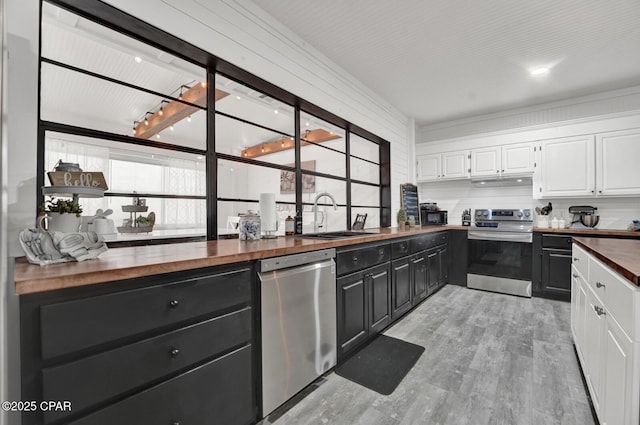 kitchen with light wood-style flooring, white cabinets, a sink, appliances with stainless steel finishes, and wooden counters