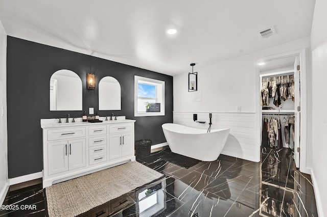 bathroom featuring double vanity, a wainscoted wall, a sink, a soaking tub, and visible vents
