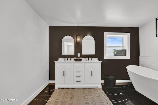 full bathroom with double vanity, baseboards, a freestanding bath, and a sink