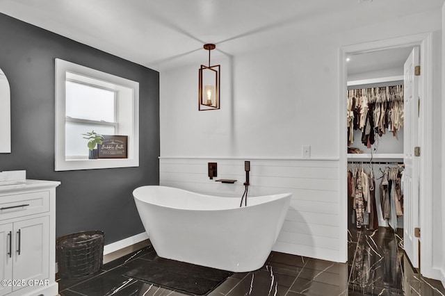 full bathroom featuring vanity, a freestanding tub, marble finish floor, a walk in closet, and wainscoting